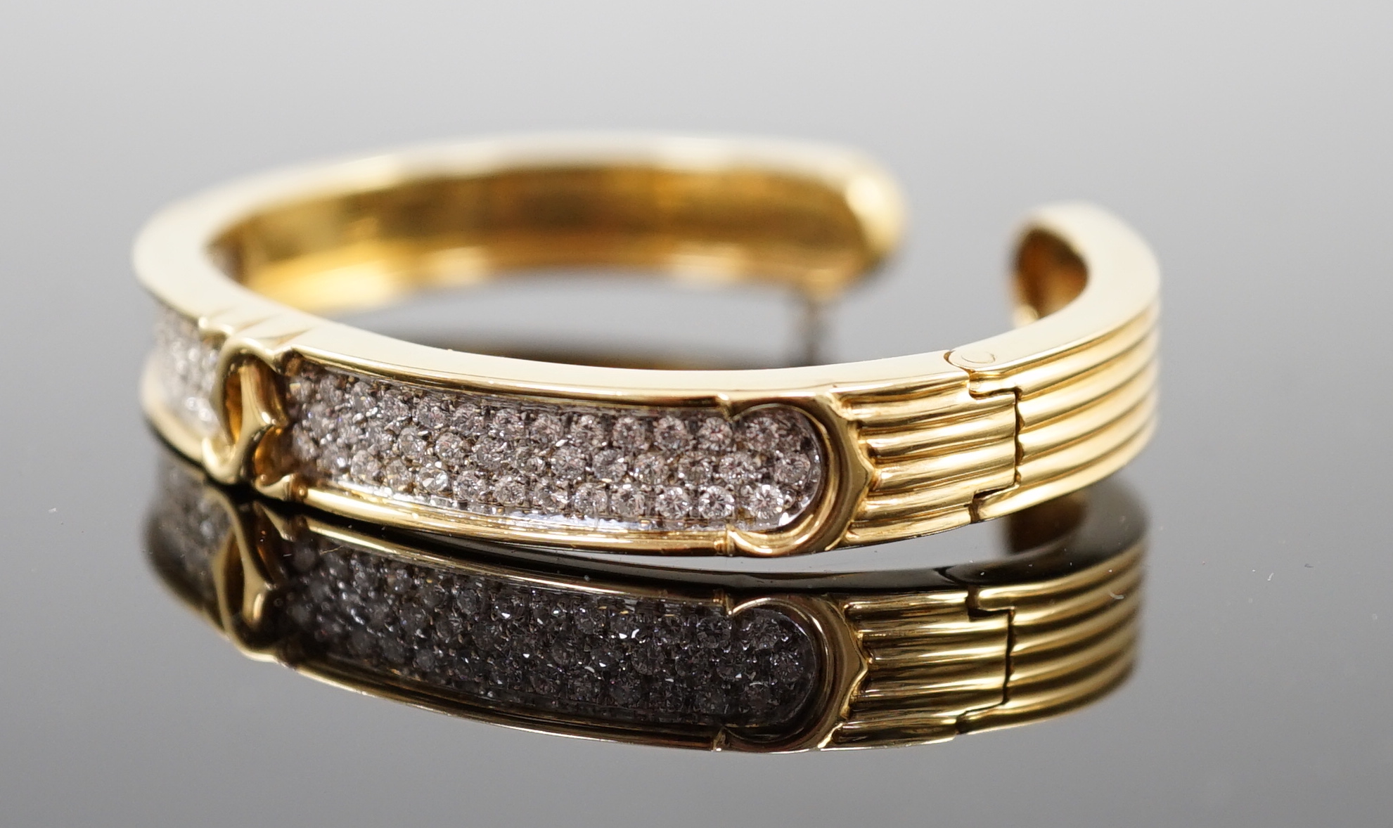 A modern 18k gold and pave set diamond Cartier open work hinged bangle